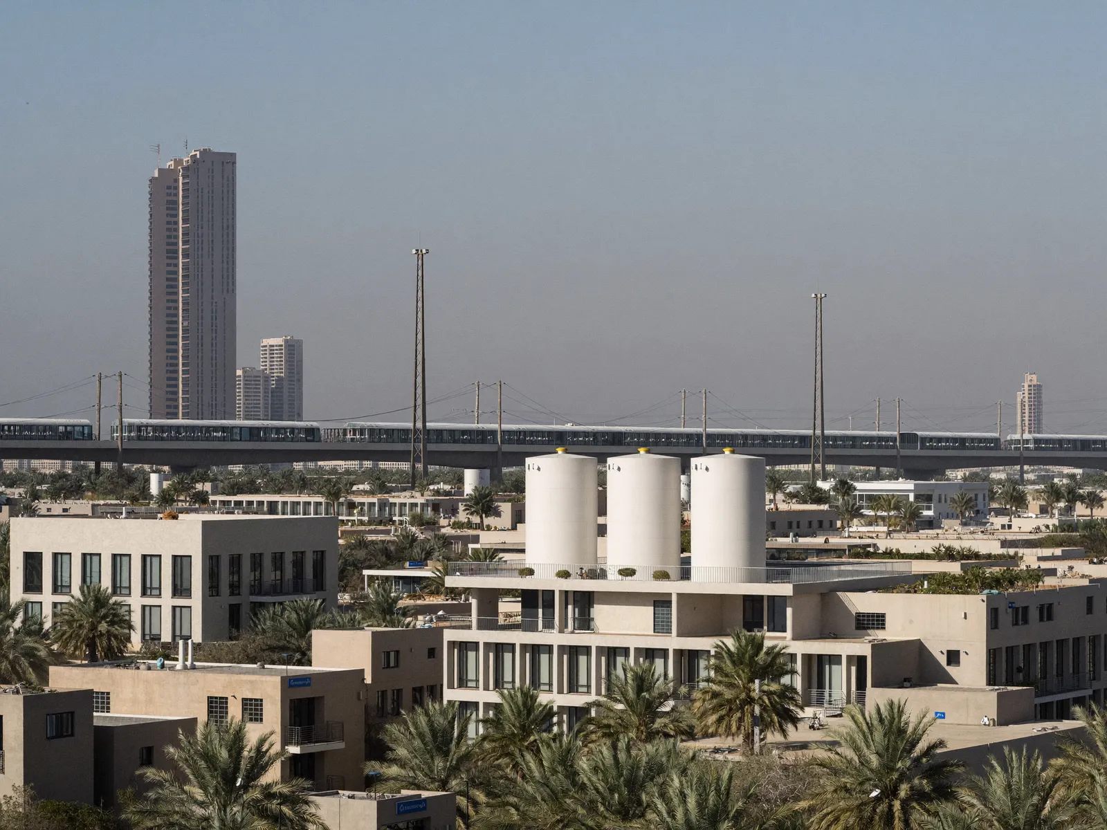 Modern townhouses in Al Furjan with a metro line in the background and tanks on the roofs