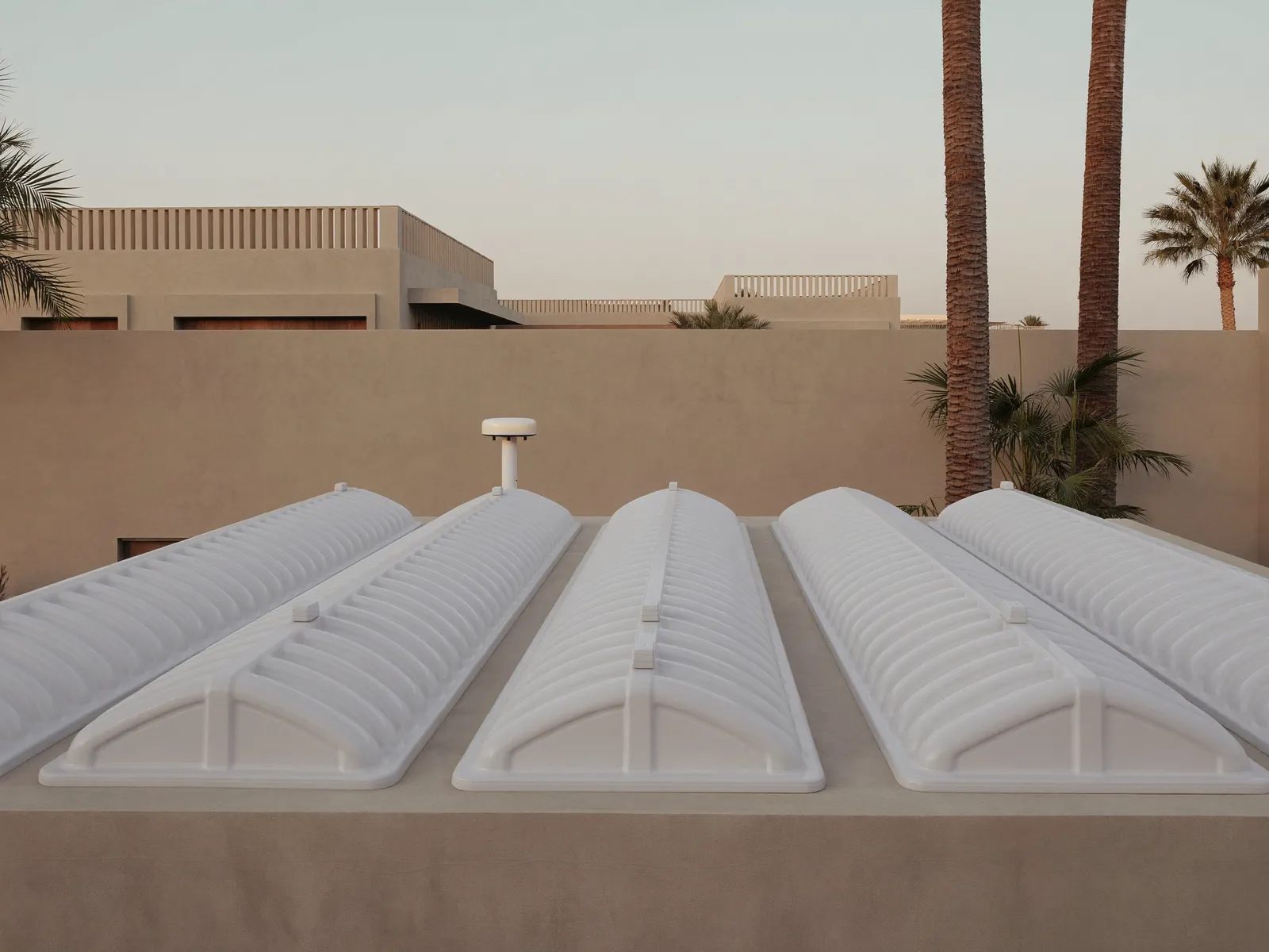 Row of white GRP water tanks on the flat roof of a Dubai villa at morning light